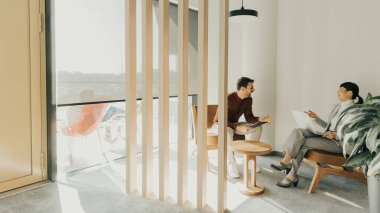 İki profesyonel şık bir ofis ortamında düşünceli bir tartışmaya giriştiler. Çağdaş koltuklarda rahatça otururken fikir alışverişinde bulundular..