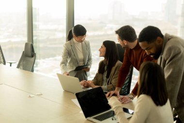 Çeşitli profesyonellerden oluşan bir grup, şık bir ofisteki masanın etrafında iş birliği yaparak, dizüstü bilgisayarlardan yararlanarak fikir ve içgörülerini paylaşıyor. Atmosfer canlı ve çekici..