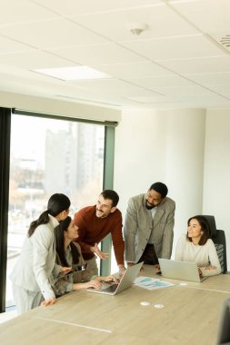Çeşitli profesyonellerden oluşan bir grup, şık bir ofisteki masanın etrafında iş birliği yaparak, dizüstü bilgisayarlardan yararlanarak fikir ve içgörülerini paylaşıyor. Atmosfer canlı ve çekici..
