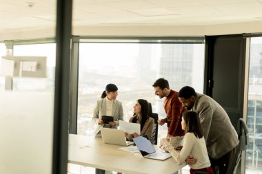 Çeşitli profesyonellerden oluşan bir grup, bir konferans masası etrafında dinamik bir beyin fırtınası yapıyor, fikirlerini paylaşıyor ve parlak bir ofis alanında dizüstü bilgisayar ve notlarla etkileşime giriyor..