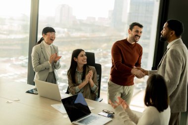 Meslektaşlar başarılı bir işbirliğini kutlamak için parlak ve çağdaş bir ofiste toplandılar. Gülümsemeler, tokalaşmalar ve alkışlar havayı doldurur, birlik ve başarılarını gösterir..