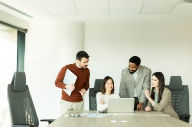 Çeşitli profesyonellerden oluşan bir grup, bir konferans masası etrafında dinamik bir beyin fırtınası yapıyor, fikirlerini paylaşıyor ve parlak bir ofis alanında dizüstü bilgisayar ve notlarla etkileşime giriyor..