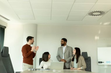 Parlak bir ofiste, çeşitli profesyonellerden oluşan bir grup dizüstü bilgisayarın etrafında toplanarak, dinamik tartışmalar, takım çalışması ve yaratıcılıkla uğraşırken içgörü ve stratejilerini paylaşıyor..