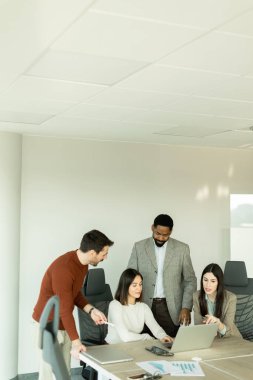 Parlak bir ofiste, çeşitli profesyonellerden oluşan bir grup dizüstü bilgisayarın etrafında toplanarak, dinamik tartışmalar, takım çalışması ve yaratıcılıkla uğraşırken içgörü ve stratejilerini paylaşıyor..