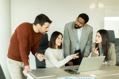 Parlak bir ofiste, çeşitli profesyonellerden oluşan bir grup dizüstü bilgisayarın etrafında toplanarak, dinamik tartışmalar, takım çalışması ve yaratıcılıkla uğraşırken içgörü ve stratejilerini paylaşıyor..