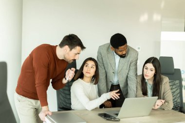 Parlak bir ofiste, çeşitli profesyonellerden oluşan bir grup dizüstü bilgisayarın etrafında toplanarak, dinamik tartışmalar, takım çalışması ve yaratıcılıkla uğraşırken içgörü ve stratejilerini paylaşıyor..