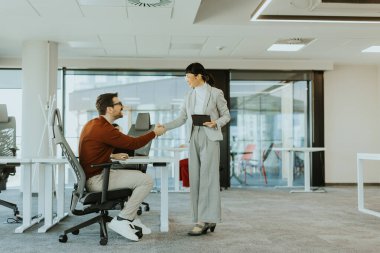 İki meslektaş, parlak ve çağdaş bir ofis ortamında el sıkışırken bir anlık bağlantının keyfini çıkarırlar. Bu da başarılı bir işbirliği ve karşılıklı saygının göstergesidir..