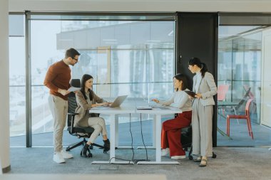 Dört profesyonel, doğal ışıkla dolu modern bir ofis ortamında dizüstü bilgisayarların etrafında dinamik bir tartışmaya girişiyor. Bir projede işbirliği yaparken fikir akışı.