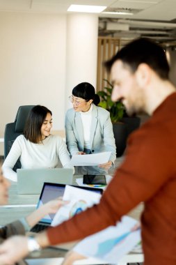 Çağdaş bir çalışma alanında, bir ekip canlı bir tartışma içine girer, büyük bir masa etrafında fikirler ve belgeler paylaşır. İfadeleri coşku ve takım çalışmasını yansıtıyor.