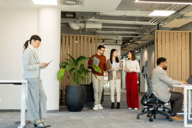 Bir grup profesyonel, dokümanları incelerken, yeşil ve çağdaş çalışma alanlarında takım çalışması ve yaratıcılığı somutlaştırırken, canlı tartışmalara girişiyor..