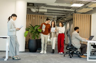 Bir grup profesyonel, dokümanları incelerken, yeşil ve çağdaş çalışma alanlarında takım çalışması ve yaratıcılığı somutlaştırırken, canlı tartışmalara girişiyor..