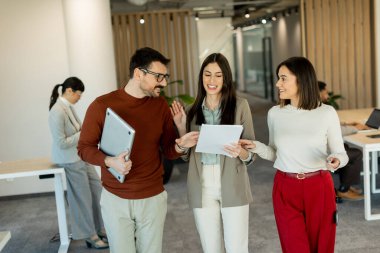 Bir grup profesyonel, dokümanları incelerken, yeşil ve çağdaş çalışma alanlarında takım çalışması ve yaratıcılığı somutlaştırırken, canlı tartışmalara girişiyor..