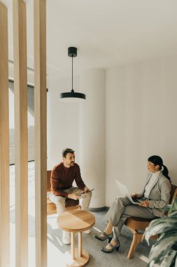 İki profesyonel şık bir ofis ortamında düşünceli bir tartışmaya giriştiler. Çağdaş koltuklarda rahatça otururken fikir alışverişinde bulundular..