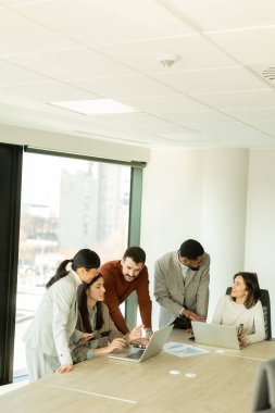 Çeşitli profesyonellerden oluşan bir grup, şık bir ofisteki masanın etrafında iş birliği yaparak, dizüstü bilgisayarlardan yararlanarak fikir ve içgörülerini paylaşıyor. Atmosfer canlı ve çekici..
