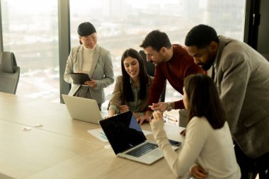 Çeşitli profesyonellerden oluşan bir grup, şık bir ofisteki masanın etrafında iş birliği yaparak, dizüstü bilgisayarlardan yararlanarak fikir ve içgörülerini paylaşıyor. Atmosfer canlı ve çekici..
