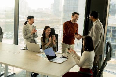 Meslektaşlar başarılı bir işbirliğini kutlamak için parlak ve çağdaş bir ofiste toplandılar. Gülümsemeler, tokalaşmalar ve alkışlar havayı doldurur, birlik ve başarılarını gösterir..