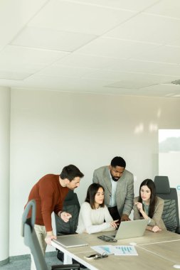 Parlak bir ofiste, çeşitli profesyonellerden oluşan bir grup dizüstü bilgisayarın etrafında toplanarak, dinamik tartışmalar, takım çalışması ve yaratıcılıkla uğraşırken içgörü ve stratejilerini paylaşıyor..