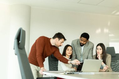 Çeşitli profesyonellerden oluşan bir grup, bir konferans masası etrafında dinamik bir beyin fırtınası yapıyor, fikirlerini paylaşıyor ve parlak bir ofis alanında dizüstü bilgisayar ve notlarla etkileşime giriyor..