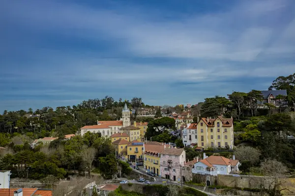 Pastel renklere boyanmış eski evler, arka planda parlak mavi bir gökyüzünde süzülen ince bulutlar gibi, Portekiz, Sintra 'nın yeşillikleri arasında uyum içinde otururlar..