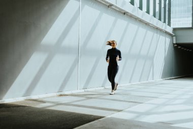 Güneş ışığı yüksek binaların arasından süzülür. Koşucu enerjik bir şekilde şehir yolunda ilerler. Gölgeler onun yanında dans eder..