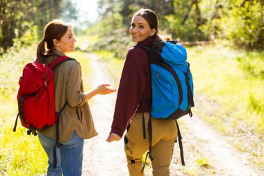 Parlak, güneşli bir günde, canlı bir yeşilliğin ortasında sakin bir orman yolunda yürürken iki arkadaş keyifli bir sohbetin tadını çıkarırlar..