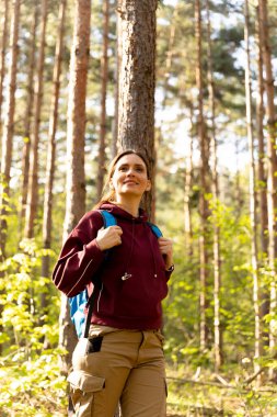 Huzurlu bir ormanda, doğa manzarası ve sesleriyle ıslanmış, günlük yürüyüş kıyafetleri ve sırt çantası giymiş genç bir kadın..