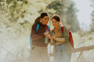 Doğanın güzelliği ve güneş ışığıyla çevrelenmiş iki kadın, hareketli yeşil ormanda neşeli bir anı paylaşıyor..