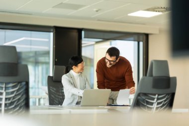 İki profesyonel, şık bir ofis çalışma alanında dizüstü bilgisayardaki bilgileri incelerken canlı bir tartışmaya girişiyor. Coşkuları takım çalışması ve yenilikleri vurguluyor.