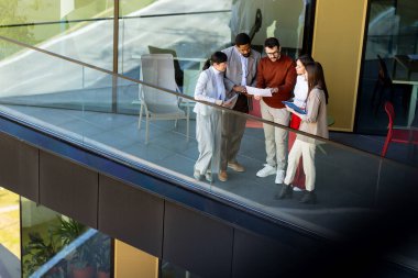 Dört profesyonel balkonda toplanıp parlak güneş ışığının tadını çıkarırken proje planlarını tartışıyorlar..