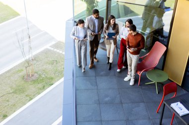 Beş profesyonelden oluşan çeşitli bir grup, lüks bir terasta dijital tabletleri incelerken canlı tartışmalara giriyorlar. Güneş ışığı kıyafetlerine neşe saçar..