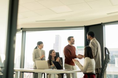 Çeşitli profesyonellerden oluşan bir grup, bir konferans masası etrafında dinamik bir beyin fırtınası yapıyor, fikirlerini paylaşıyor ve parlak bir ofis alanında dizüstü bilgisayar ve notlarla etkileşime giriyor..