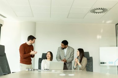 Parlak bir ofiste, çeşitli profesyonellerden oluşan bir grup dizüstü bilgisayarın etrafında toplanarak, dinamik tartışmalar, takım çalışması ve yaratıcılıkla uğraşırken içgörü ve stratejilerini paylaşıyor..