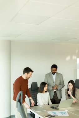 Parlak bir ofiste, çeşitli profesyonellerden oluşan bir grup dizüstü bilgisayarın etrafında toplanarak, dinamik tartışmalar, takım çalışması ve yaratıcılıkla uğraşırken içgörü ve stratejilerini paylaşıyor..