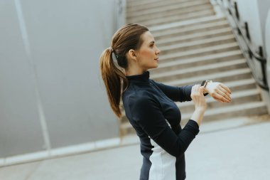 Spor kıyafetleri içindeki odaklanmış birey, sabah saatlerinde canlı bir şehir ortamında açık havada egzersiz yapmaya hazır olarak akıllı saatini ayarlar..