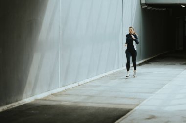 Dar, güneşli bir koridorda koşan bir kadın huzurlu bir şehir ortamında canlandırıcı bir sabah koşusunun tadını çıkarıyor..