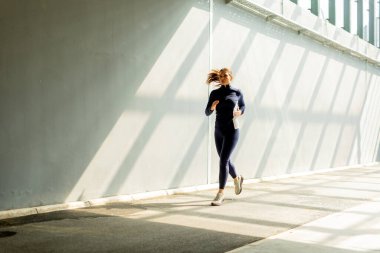 Kendini adamış bir koşucu parlak, güneşli bir patika boyunca yarışır. Şehrin hareketli kalbine çağdaş binalarla çevrili uzun gölgeler bırakır..