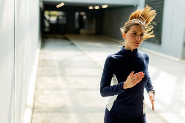 Kararlı bir kadın modern kentsel alanda koşar, saçları süzülürken koşusunun ritmini kucaklar, zarif bir mimarinin ortasında..