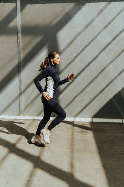 Kararlı bir koşucu, kentsel bir ortamda çarpıcı ışık ve gölge desenleriyle çevrili bir sabah antrenmanının zorluklarını kucaklar..