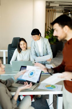 Çağdaş bir ofiste, çeşitli bir ekip laptoplardaki rapor ve çizelgeleri incelerken, işbirliği ve yenilikçi fikirleri desteklerken, canlı bir tartışmaya girişiyor..
