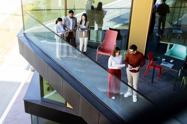 Dört profesyonel balkonda toplanıp parlak güneş ışığının tadını çıkarırken proje planlarını tartışıyorlar..