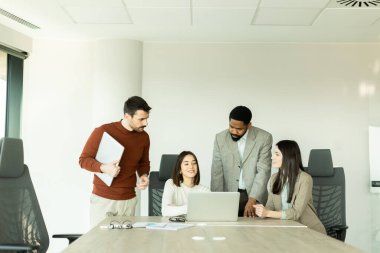 Parlak bir ofiste, çeşitli profesyonellerden oluşan bir grup dizüstü bilgisayarın etrafında toplanarak, dinamik tartışmalar, takım çalışması ve yaratıcılıkla uğraşırken içgörü ve stratejilerini paylaşıyor..