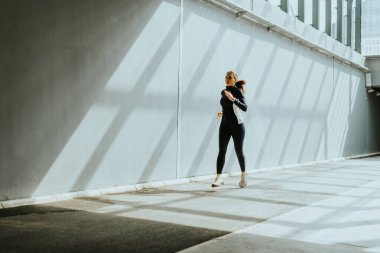 Kendini adamış bir koşucu parlak, güneşli bir patika boyunca yarışır. Şehrin hareketli kalbine çağdaş binalarla çevrili uzun gölgeler bırakır..