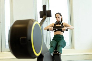 Kararlı bir kadın parlak, şık bir spor salonunda kürek çekiyor, gücünü gösteriyor ve spor salonuna odaklanıyor..