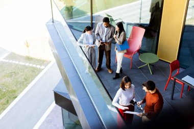 Bir grup profesyonel, çağdaş bir ofis balkonunun havadar alanının keyfini çıkarırken bir projede işbirliği yapıyor. Güneş ışığı geniş pencerelerden süzülerek canlı tartışmalarını geliştirir..