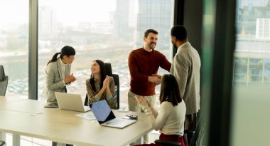 Çeşitli profesyonellerden oluşan bir grup, bir konferans masası etrafında dinamik bir beyin fırtınası yapıyor, fikirlerini paylaşıyor ve parlak bir ofis alanında dizüstü bilgisayar ve notlarla etkileşime giriyor..