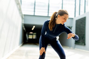 Antrenmanına odaklanmış, kendini işine adamış bir atlet, öğleden sonra saatinde şık bir iç mekan antrenman alanında saatini kontrol ediyor..