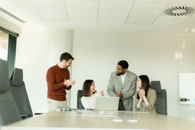 Parlak bir ofiste, çeşitli profesyonellerden oluşan bir grup dizüstü bilgisayarın etrafında toplanarak, dinamik tartışmalar, takım çalışması ve yaratıcılıkla uğraşırken içgörü ve stratejilerini paylaşıyor..
