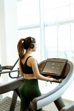 Adanmış bir birey koşu bandında kardiyo çalışmasına katılır, kararlılığını gösterir ve parlak ve havadar bir spor salonunda odaklanır..