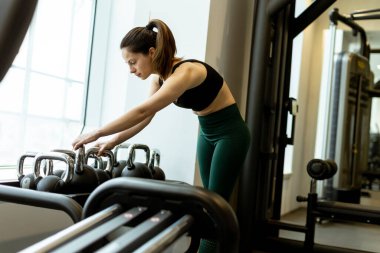Odaklanmış birey, iyi aydınlatılmış bir spor salonunda kettlebells ayarlar, bir sabah eğitim oturumu sırasında azim ve zindelik sunar.