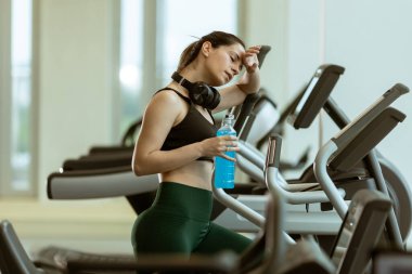 Terleyen ve kararlı genç bir kadın, iyi ışıklandırılmış bir spor salonunda canlandırıcı bir egzersizden sonra biraz soluklanır..